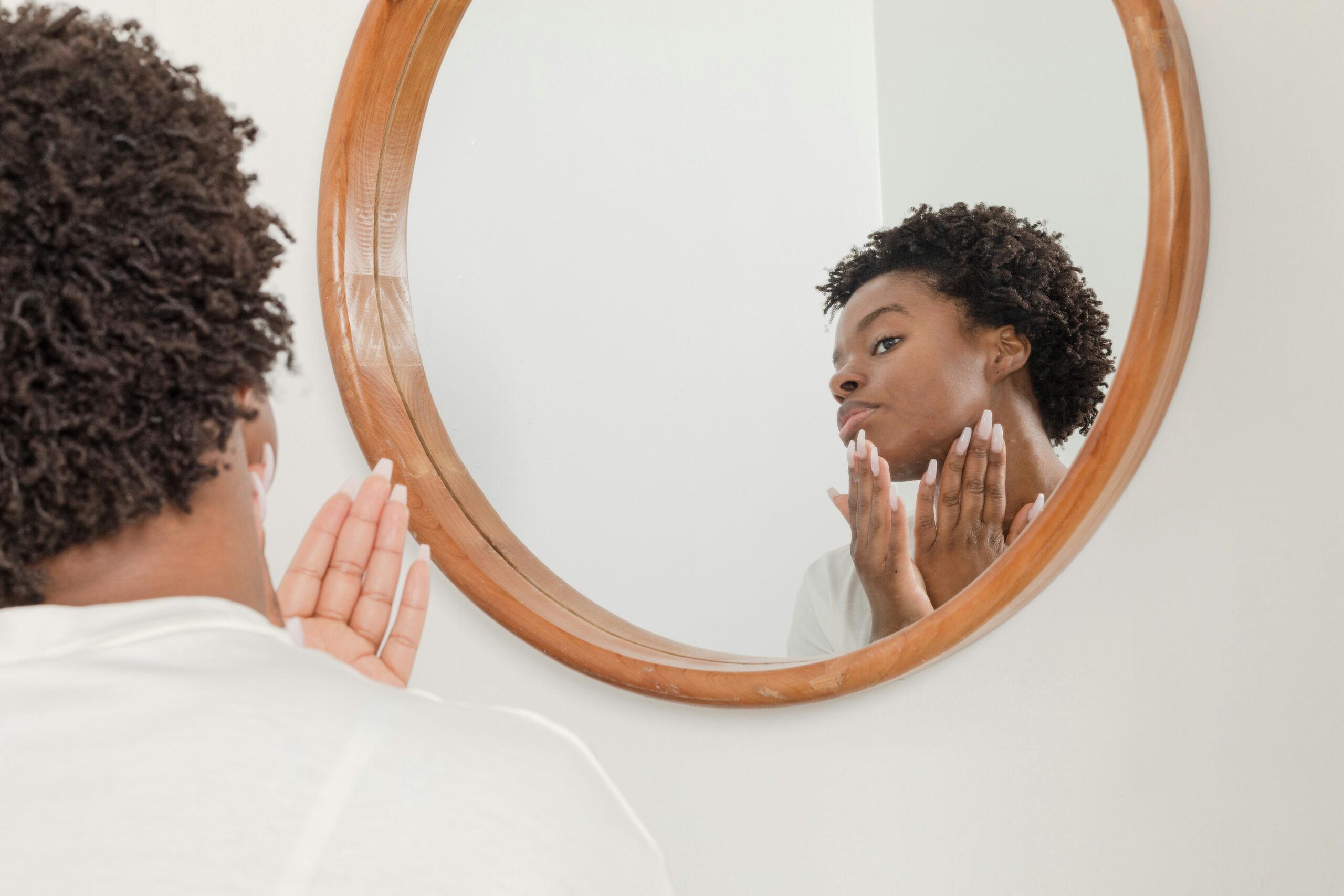 Woman examining her skin closely in a mirror, checking for acne scars and marks